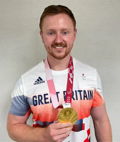 Dr Tom O'Brien holding a Paralympic medal.